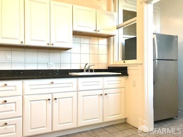 kitchen with freestanding refrigerator, white cabinetry, dark countertops, and light tile patterned floors