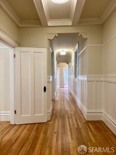 hall featuring a decorative wall, wood finished floors, crown molding, and beam ceiling
