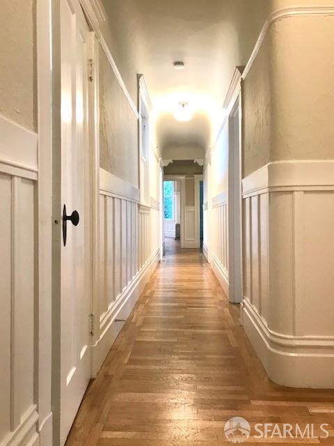 corridor featuring a decorative wall, hardwood / wood-style flooring, and wainscoting