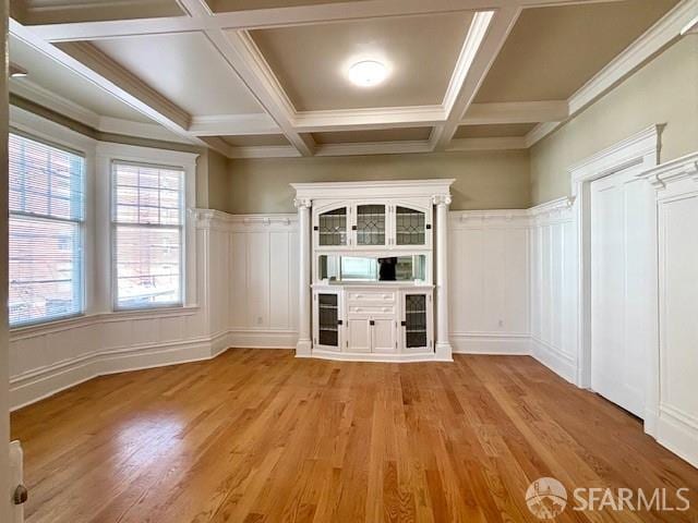 unfurnished room featuring a decorative wall, light wood-style flooring, beam ceiling, coffered ceiling, and a wainscoted wall