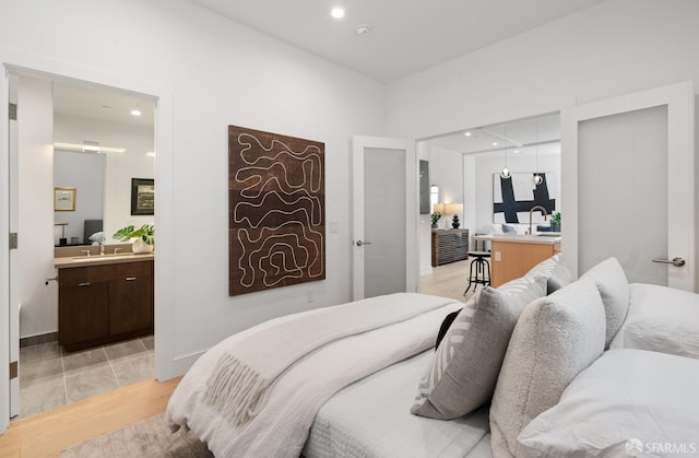 bedroom with ensuite bathroom, light hardwood / wood-style floors, and sink