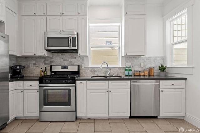 kitchen featuring tasteful backsplash, stainless steel appliances, sink, light tile patterned floors, and white cabinetry