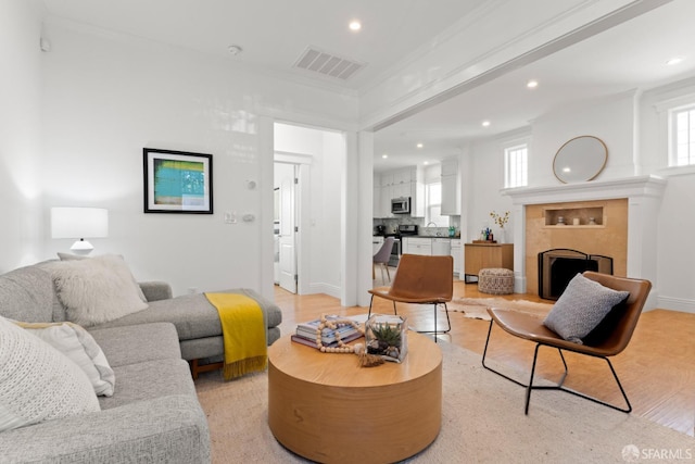 living room featuring light hardwood / wood-style floors, sink, crown molding, and a tile fireplace