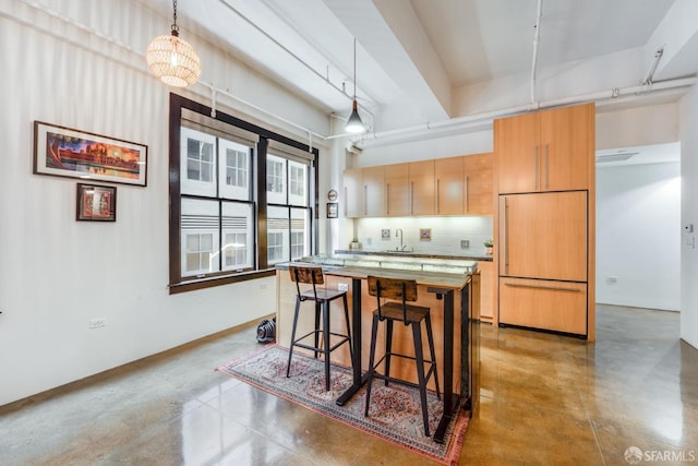 kitchen featuring pendant lighting, paneled built in fridge, sink, backsplash, and a breakfast bar area