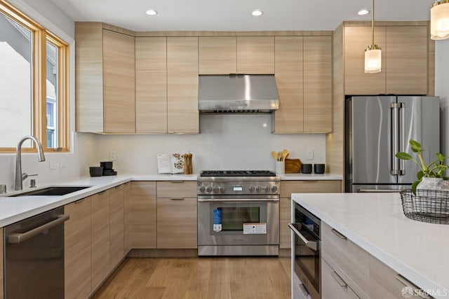 kitchen with premium appliances, range hood, a sink, light brown cabinetry, and recessed lighting