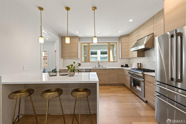 kitchen featuring stainless steel appliances, under cabinet range hood, a sink, a breakfast bar, and a peninsula