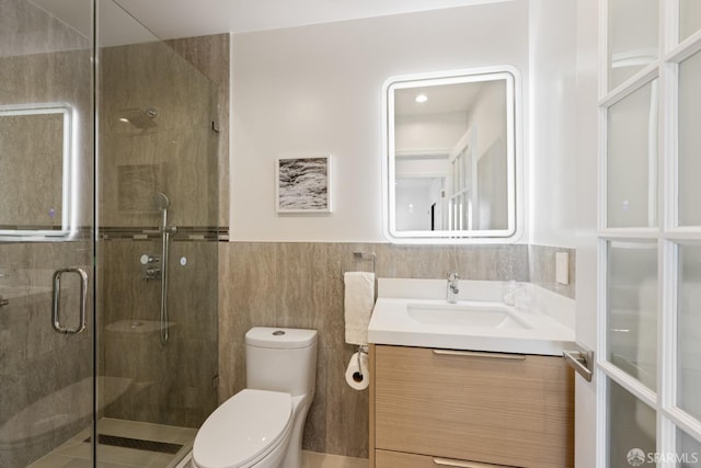 full bath featuring toilet, a shower stall, vanity, tile walls, and wainscoting