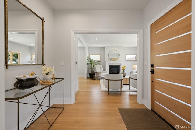 entryway featuring light wood-style floors, plenty of natural light, a glass covered fireplace, recessed lighting, and baseboards