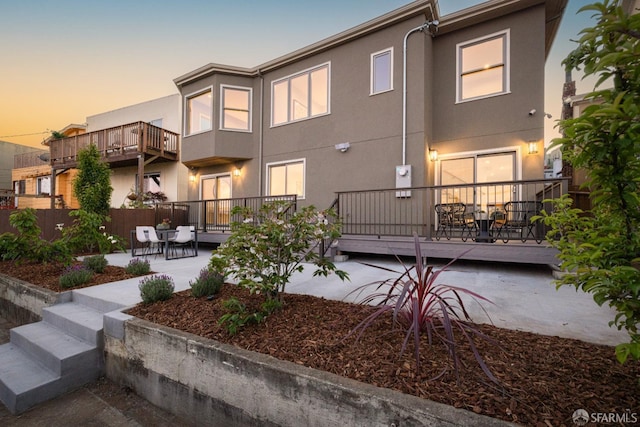 back of property at dusk featuring a patio area, stucco siding, fence, and a deck