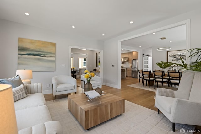 living area featuring a barn door, light wood-type flooring, recessed lighting, and baseboards