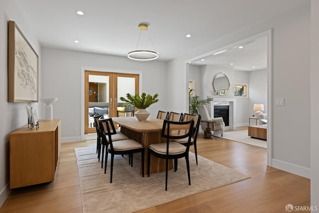 dining space with recessed lighting, light wood-type flooring, baseboards, a glass covered fireplace, and french doors