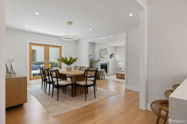 dining room featuring french doors, light wood-style flooring, recessed lighting, a fireplace, and baseboards