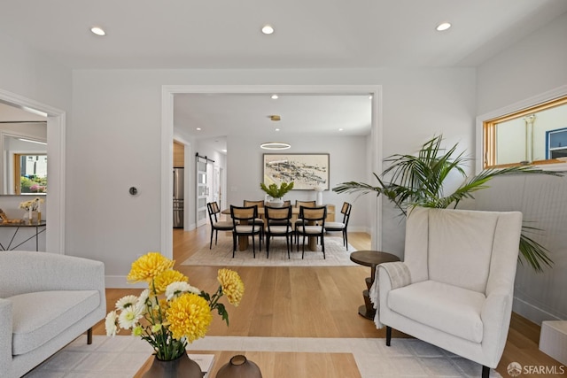 living room with light wood-type flooring, recessed lighting, a barn door, and baseboards