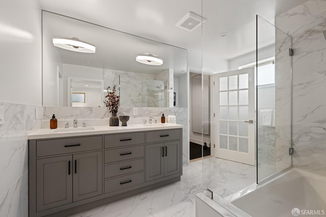 bathroom featuring marble tiled flooring, a marble finish shower, tile walls, and double vanity