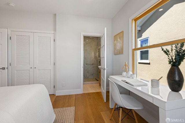 bedroom with light wood-style floors, a desk, a closet, baseboards, and connected bathroom