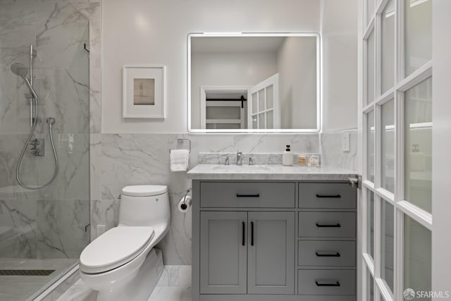 bathroom with toilet, a marble finish shower, tile walls, vanity, and a wainscoted wall