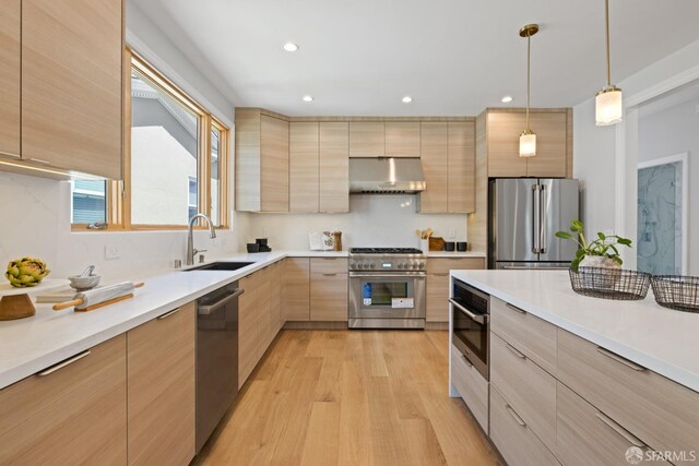kitchen featuring stainless steel appliances, a sink, under cabinet range hood, light brown cabinetry, and modern cabinets