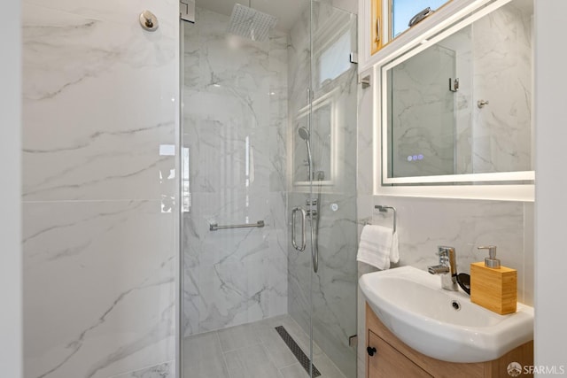 bathroom with a marble finish shower, vanity, and tile walls