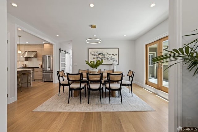 dining area with a barn door, light wood-type flooring, recessed lighting, and baseboards