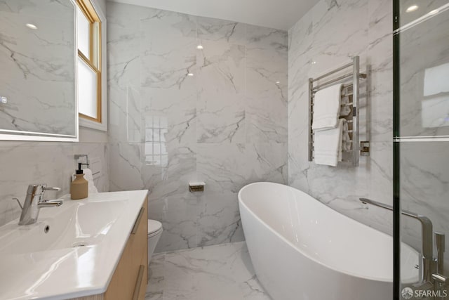 full bathroom with vanity, a freestanding tub, tile walls, a towel warming rack, and marble tiled floors
