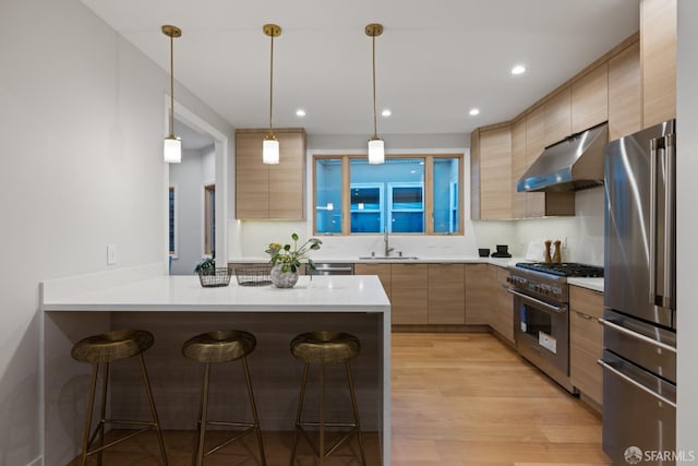kitchen featuring premium appliances, under cabinet range hood, modern cabinets, a sink, and a kitchen bar