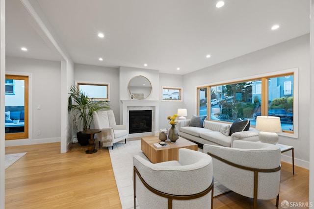 living room with light wood finished floors, baseboards, a glass covered fireplace, recessed lighting, and healthy amount of natural light