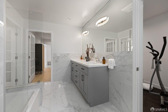 bathroom with tile walls, vanity, wainscoting, marble tiled flooring, and a tub to relax in