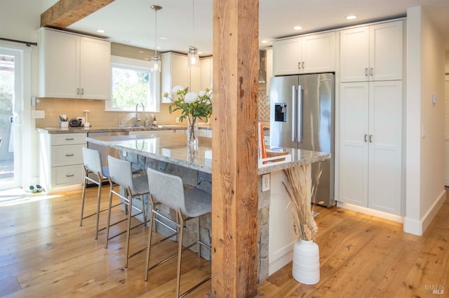 kitchen featuring a kitchen breakfast bar, stainless steel refrigerator with ice dispenser, backsplash, a kitchen island, and light wood-style floors
