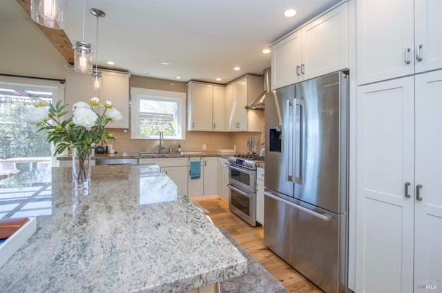 kitchen with light wood-style flooring, a sink, wall chimney range hood, stainless steel appliances, and tasteful backsplash
