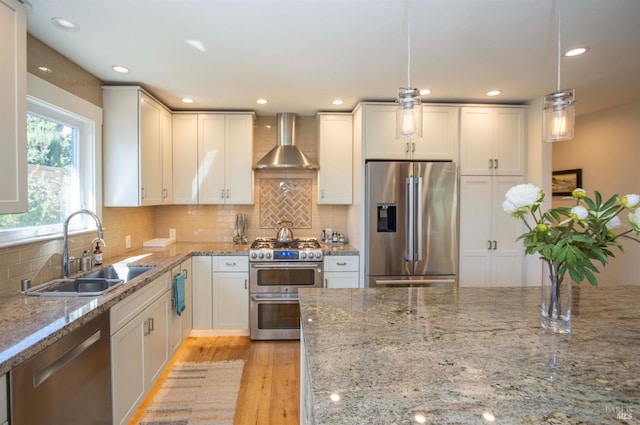 kitchen featuring appliances with stainless steel finishes, light stone counters, a sink, wall chimney exhaust hood, and light wood-type flooring