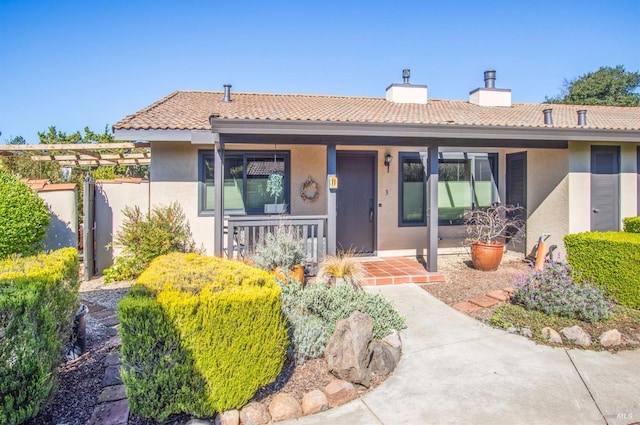 ranch-style house featuring covered porch, stucco siding, a tile roof, and a chimney