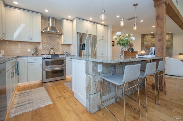 kitchen featuring light stone counters, wall chimney exhaust hood, recessed lighting, decorative backsplash, and appliances with stainless steel finishes