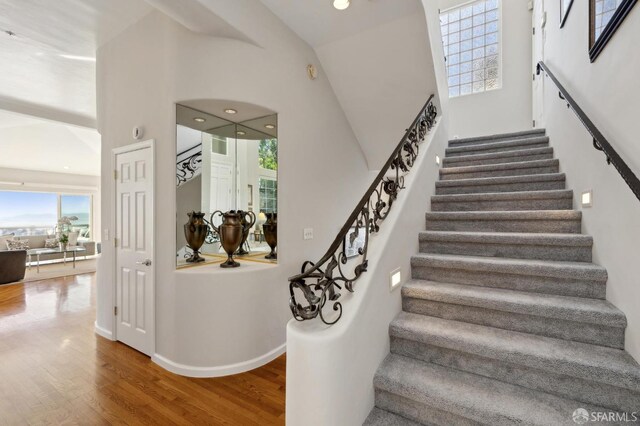 stairway with a high ceiling, baseboards, and wood finished floors