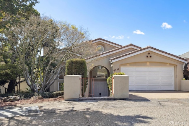 mediterranean / spanish house featuring a garage, a tile roof, a gate, and stucco siding