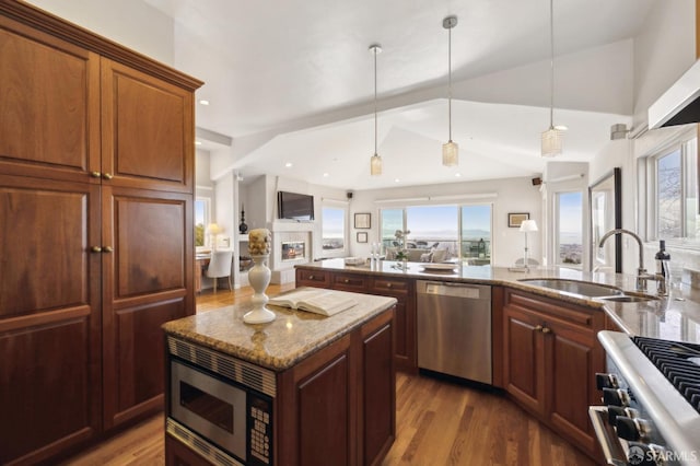 kitchen featuring light stone counters, appliances with stainless steel finishes, open floor plan, vaulted ceiling, and a sink