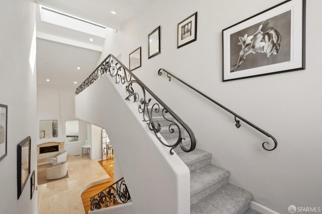 stairs featuring a fireplace, a high ceiling, and recessed lighting