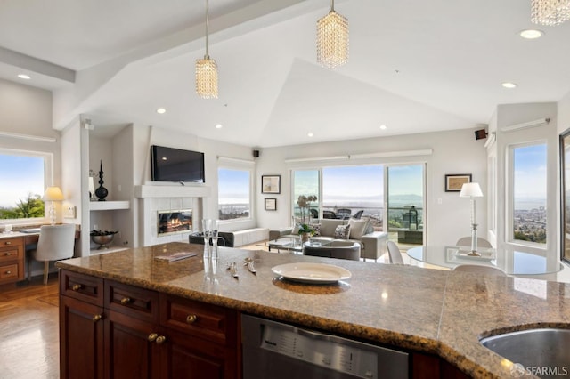 kitchen with vaulted ceiling, a tile fireplace, open floor plan, and dishwasher