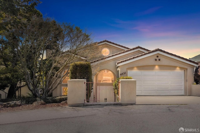 mediterranean / spanish home featuring a garage, driveway, a tiled roof, and stucco siding