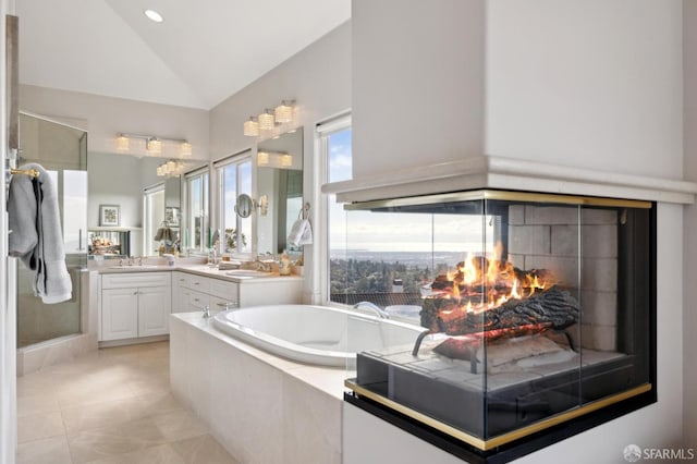 bathroom with lofted ceiling, tile patterned floors, a garden tub, vanity, and a multi sided fireplace