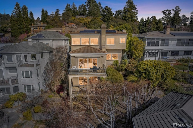 rear view of house with stucco siding, a balcony, and solar panels