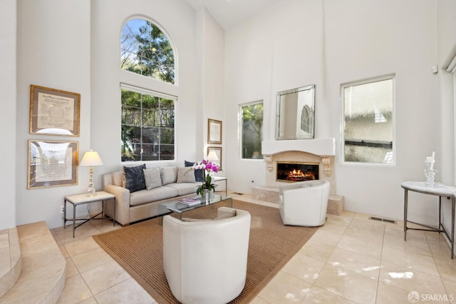 living room featuring plenty of natural light, visible vents, a fireplace, and a high ceiling