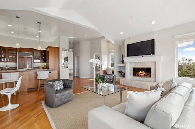 living area with recessed lighting, a tiled fireplace, light wood-style floors, vaulted ceiling, and baseboards