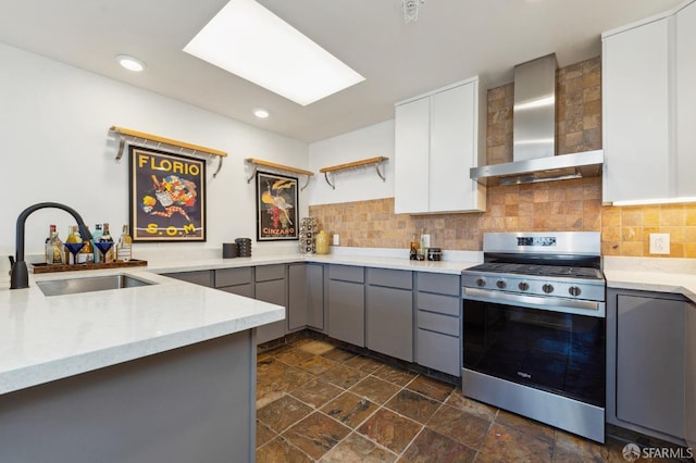 kitchen featuring stainless steel gas range oven, wall chimney exhaust hood, gray cabinetry, sink, and white cabinetry