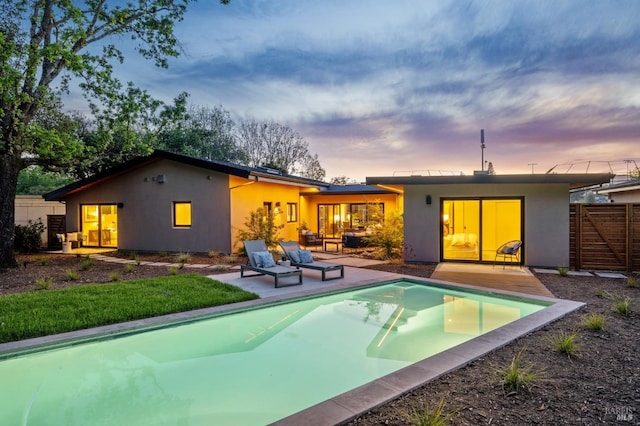 back of house at dusk with a patio area, an outdoor pool, stucco siding, and fence
