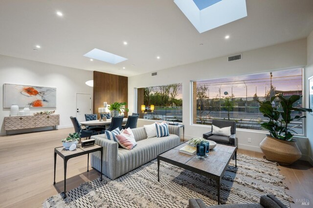 living area featuring a skylight, light wood finished floors, visible vents, and recessed lighting