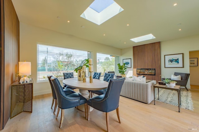 dining space featuring a skylight, light wood-type flooring, baseboards, and a healthy amount of sunlight