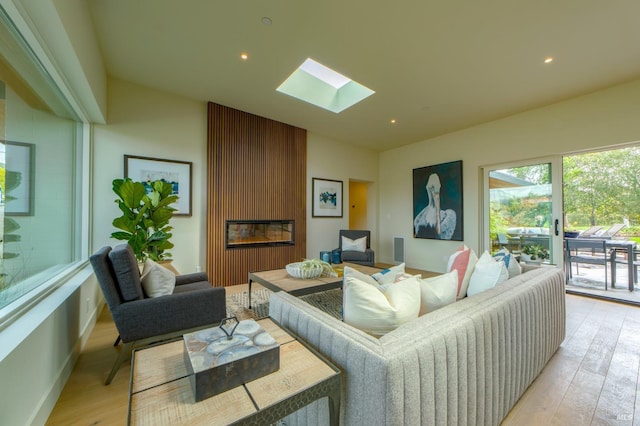 living room with a skylight, recessed lighting, a fireplace, and light wood-type flooring