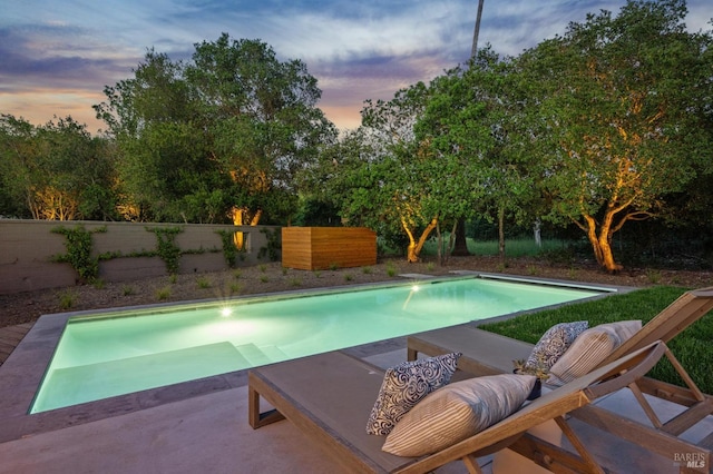 pool at dusk with a fenced backyard, a fenced in pool, and a patio