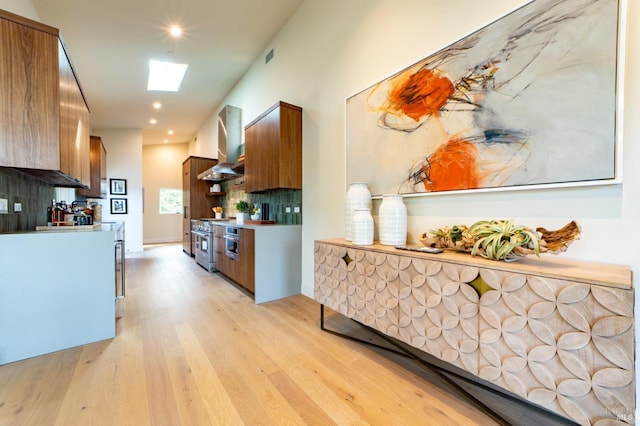 kitchen featuring brown cabinetry, high end range, extractor fan, and light wood-style floors