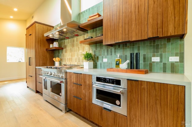 kitchen featuring wall chimney exhaust hood, light wood-type flooring, open shelves, stainless steel appliances, and brown cabinets